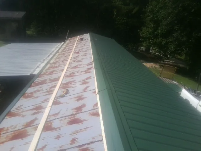 Old rusted panels beside newly installed green metal roofing — Wind Damage Roof Repair by Roofing Brothers in Wilson